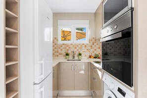 A compact kitchen with a built-in oven, a microwave, and a washing machine. - Villa Campanilla - Plusholidays (Calpe)