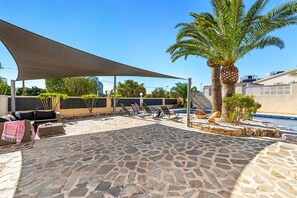 A stone patio with outdoor furniture, a palm tree, and a swimming pool. - Villa Campanilla - Plusholidays (Calpe)