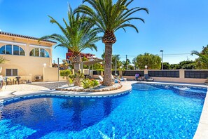 A swimming pool with palm trees, lounge chairs, and a building with large windows.