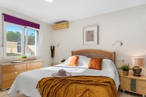 Quarto com cama, mesas de cabeceira, janela, ar condicionado e luminária na parede.