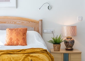 A neatly arranged bedroom with a bed, a bedside lamp, a wall-mounted light, a power outlet, and a decorative plant. - Villa Campanilla - Plusholidays (Calpe)