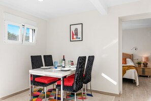 A dining area with a table set for four, chairs with red cushions, a framed picture on the wall, and a window with curtains.