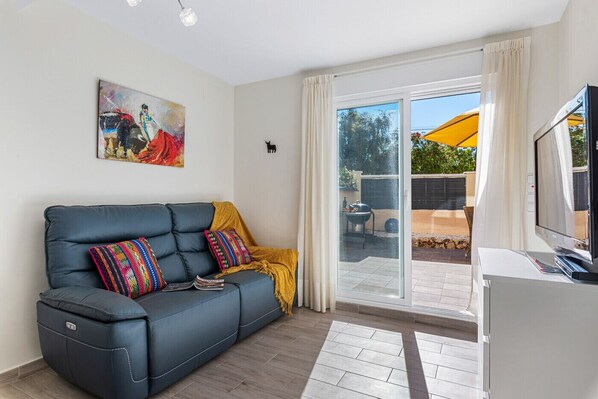 A modern living room with a sofa, colorful cushions, a television, and a sliding glass door leading to an outdoor area.