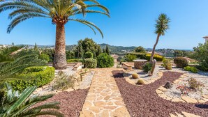 Ein angelegter Garten mit Palmen, einem Kiesweg und Blick auf die umliegende Landschaft.