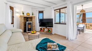 Ein Wohnzimmer mit Kamin, Sofa, Fernseher und einem Balkon mit Gartenmöbeln.