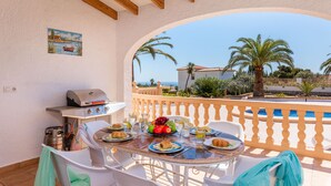 Eine Terrasse mit Tisch für zwei Personen, einem Grill und Blick auf das Meer und Palmen.