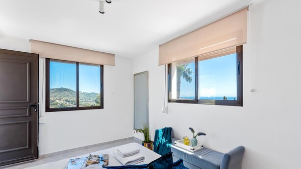 Ein Hotelzimmer mit einem Bett, einem Schreibtisch, einem Stuhl, einem Fenster mit Meerblick und einer Tür.