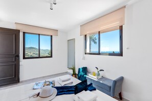 A hotel room with a bed, a desk, a chair, a window with a view of the sea, and a door. - Villa Meile - PlusHolidays (Calpe)