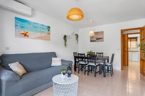 A modern living room with a grey sofa, a dining table with chairs, and a white coffee table with two wine glasses. - Apartamento Zeus 6 - PlusHolidays (Calpe)