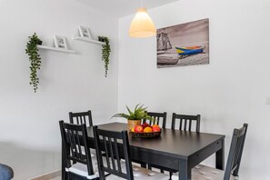 A dining area with a dark wooden table, four chairs, a fruit bowl, and a pendant light. - Apartamento Zeus 6 - PlusHolidays (Calpe)