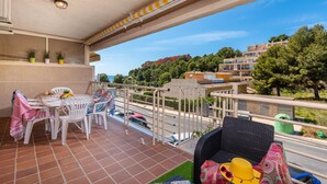 A balcony with a table and chairs, a wicker chair, and a view of the surrounding area including buildings and trees. - Apartamento Zeus 6 - PlusHolidays (Calpe)