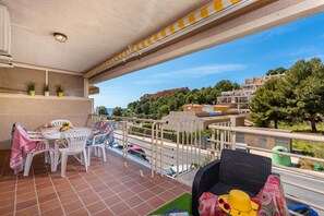 Ein Balkon mit Tisch und Stühlen, ein Korbstuhl und Blick auf die Umgebung mit Gebäuden und Bäumen.