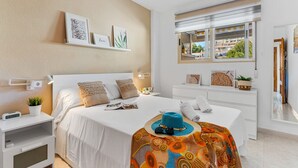 A modern hotel room with a large bed, bedside tables, a desk, and a window with a view of buildings. - Apartamento Zeus 6 - PlusHolidays (Calpe)