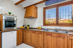 A kitchen with wooden cabinets, a stainless steel oven, a window with decorative iron bars, and a view of buildings outside.