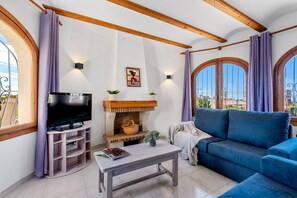 A living room with a television, fireplace, sofa, and large windows.