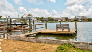 A waterfront dock with a bench, wooden walkways, and houses in the background.