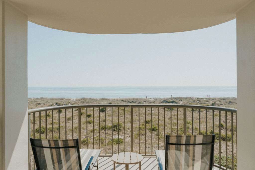 Ein Balkon mit Blick auf den Strand, zwei Stühle und ein kleiner Tisch.