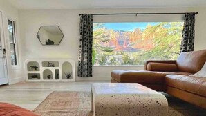 A living room with a large window, a brown leather sofa, a red sofa, and a white ottoman.