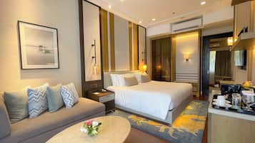 A hotel room with a sofa, two beds, a coffee table with flowers, a framed picture, and a mirror.