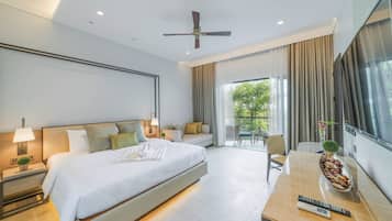 A modern hotel room with a large bed, a desk with a remote control, and a view of greenery outside.