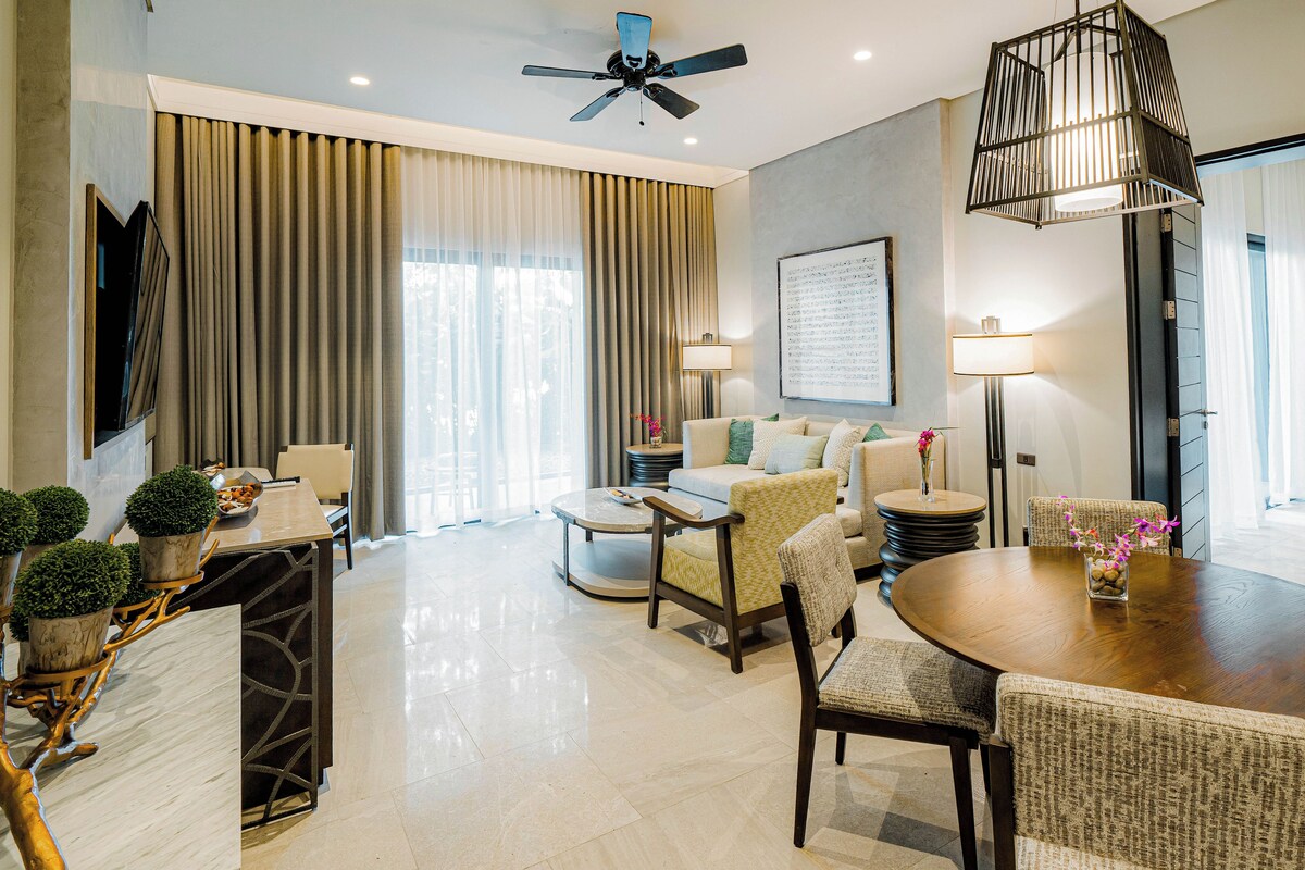 A modern hotel room with a dining area, a sofa set, a ceiling fan, and a large window with curtains.