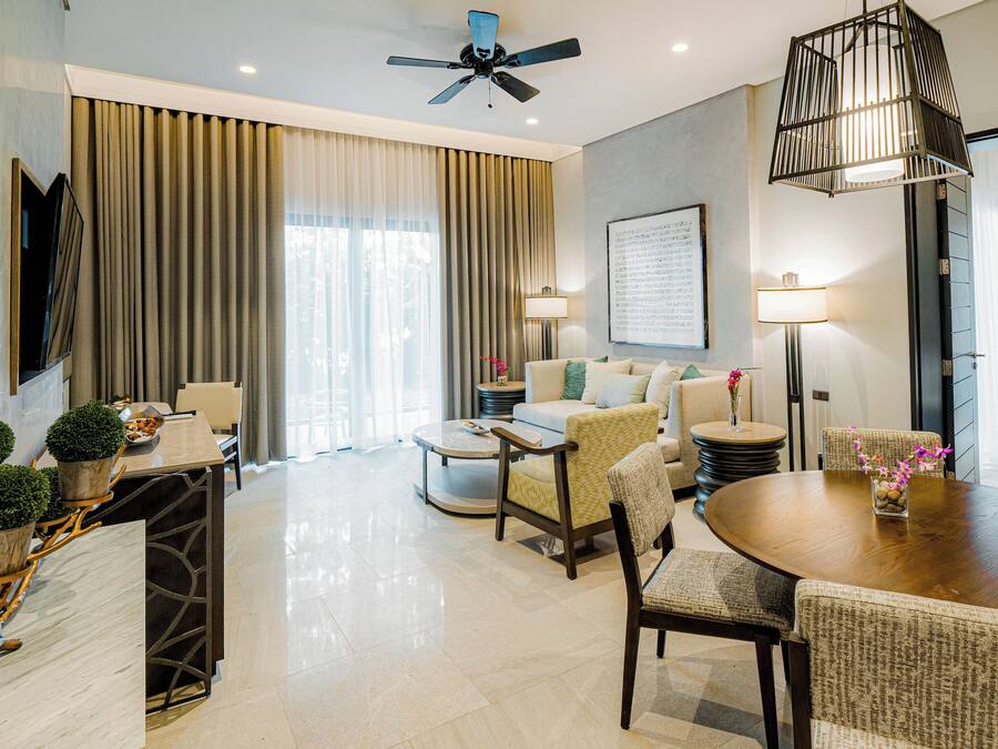 Een moderne hotelkamer met een zithoek, een loungeset, een plafondventilator en een groot raam met gordijnen.