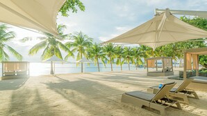 A beachside lounge area with sun loungers and umbrellas, palm trees, and a view of the sea. - Discovery Samal (Samal)