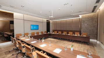 Un salón de conferencias con una larga mesa, sillas, una pantalla de televisión y un diseño de techo moderno.