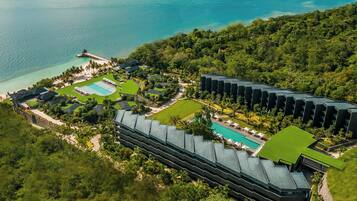 An aerial view of a resort with multiple swimming pools, lush greenery, and a beach area.