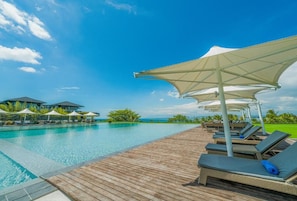 A poolside area with lounge chairs and umbrellas, a wooden deck, and a view of the ocean.
