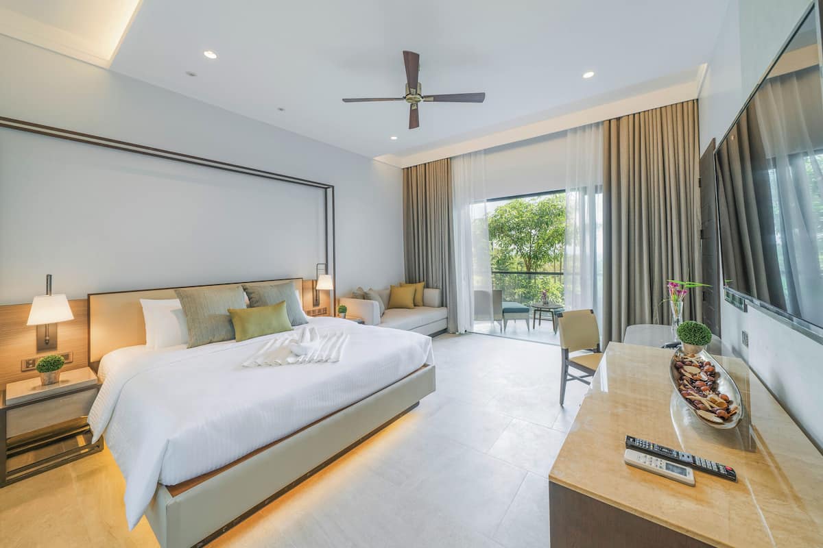 Quarto de hotel moderno com uma cama grande, uma escrivaninha com controle remoto e vista para o verde lá fora.