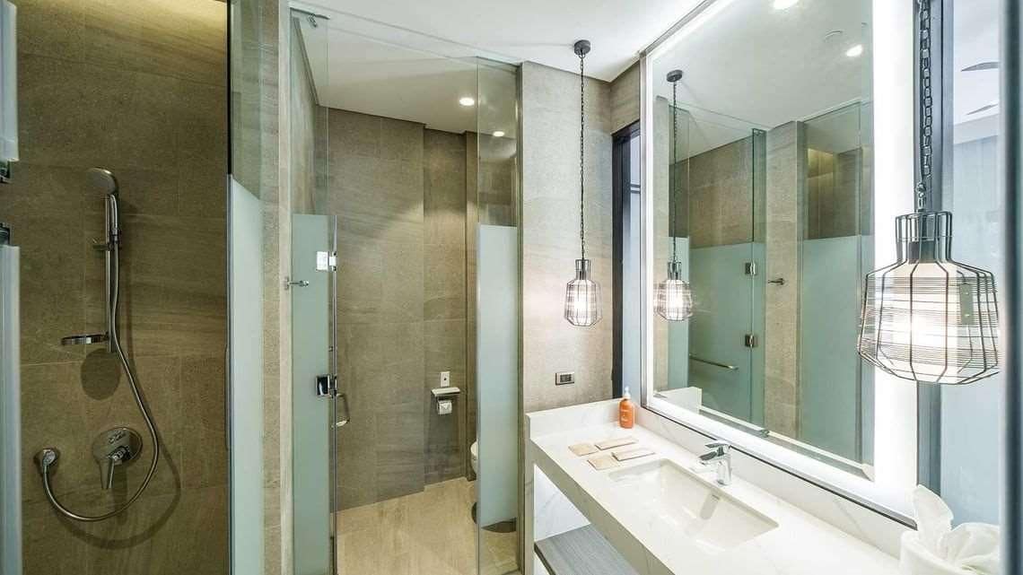 A modern bathroom with a glass-enclosed shower, a large mirror, and pendant lights.