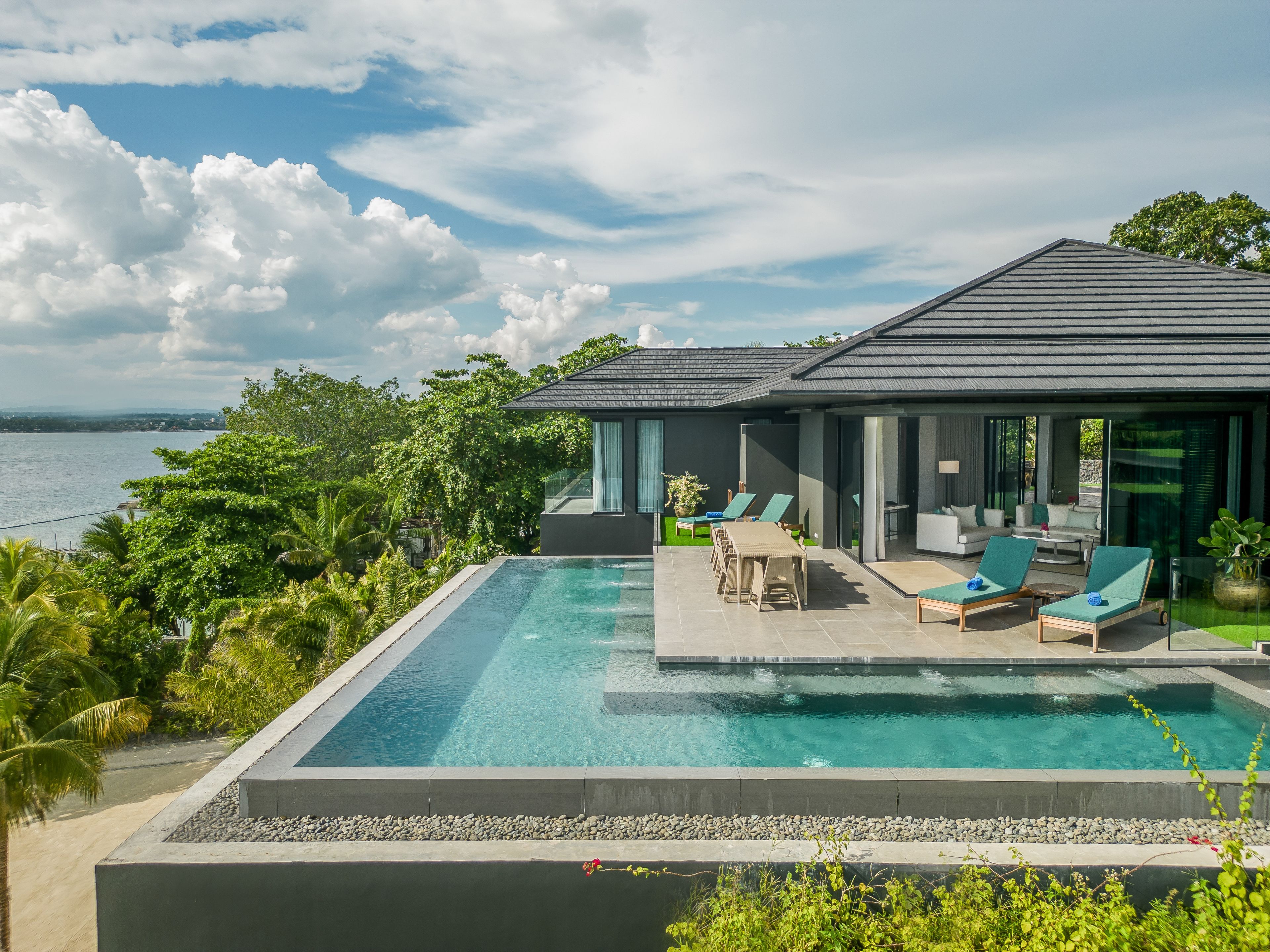 A modern house with a pool, outdoor seating, and a view of the sea.