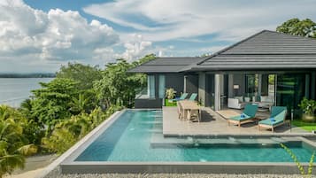 A modern house with a pool, outdoor seating, and a view of the sea.