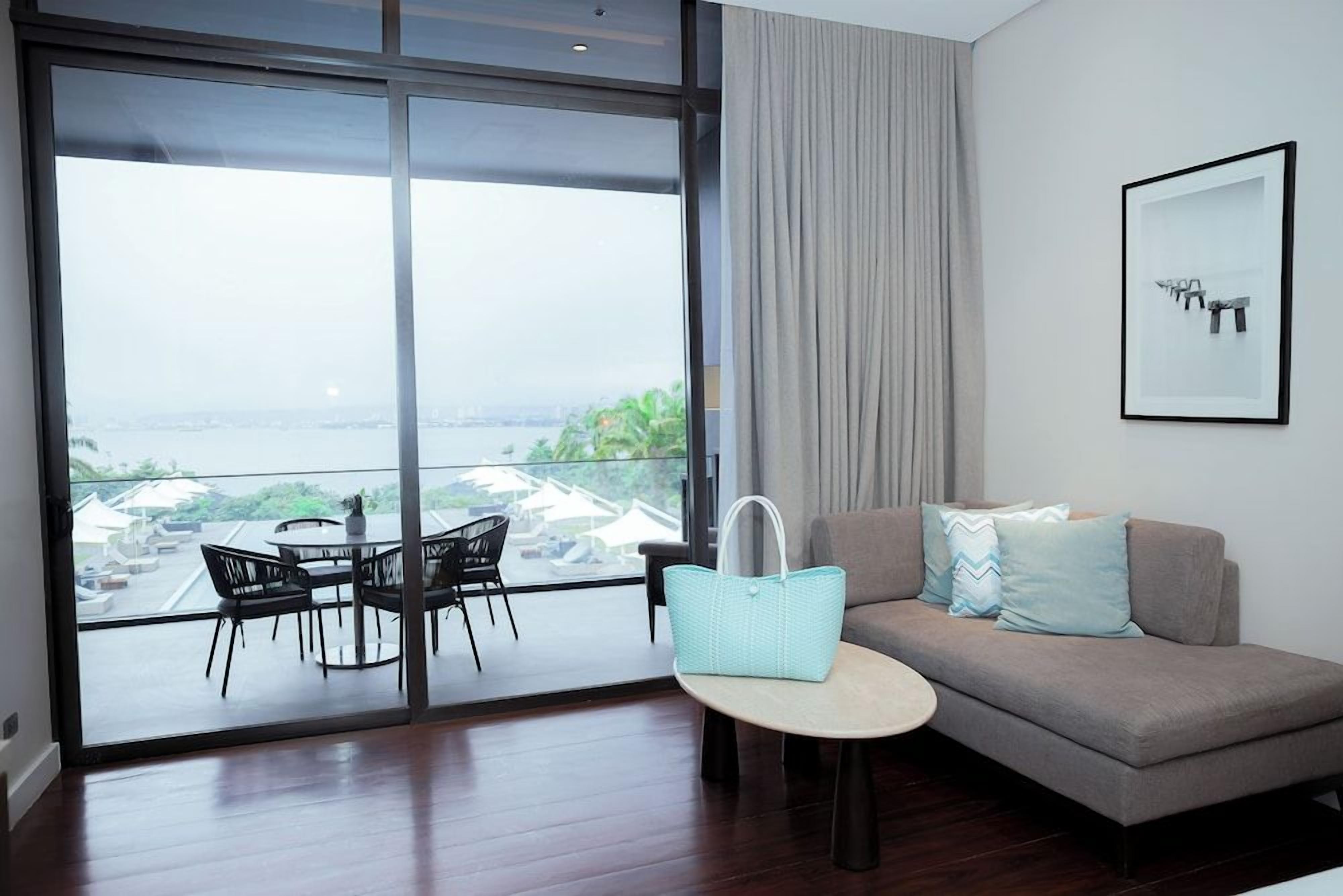 A modern living room with a sofa, a small round table, and a view through large glass doors to an outdoor area with a dining set.
