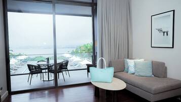 A modern living room with a sofa, a small round table, and a view through large glass doors to an outdoor area with a dining set.
