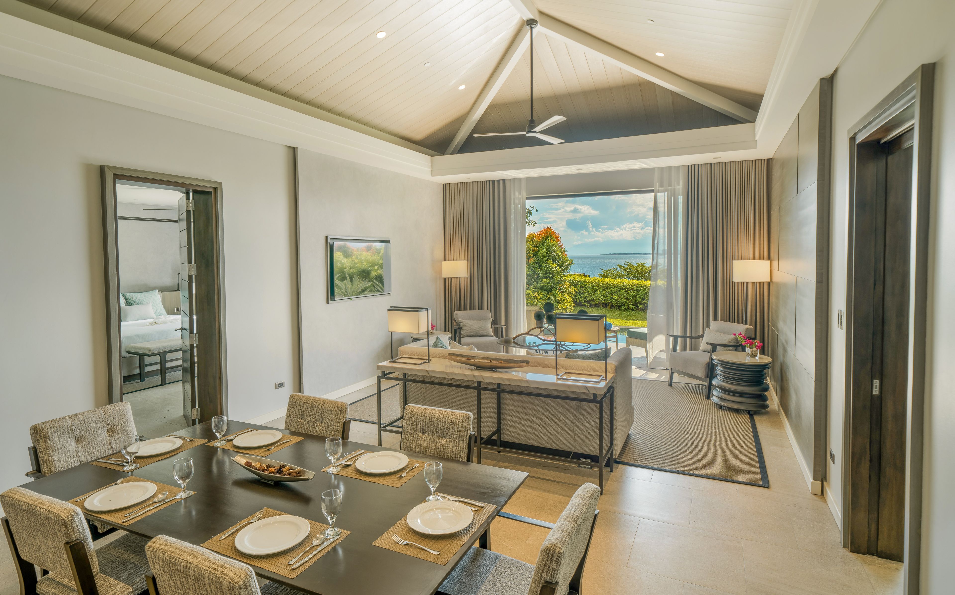 A modern dining area with a large table set for six, a ceiling fan, and a view of the outdoors.