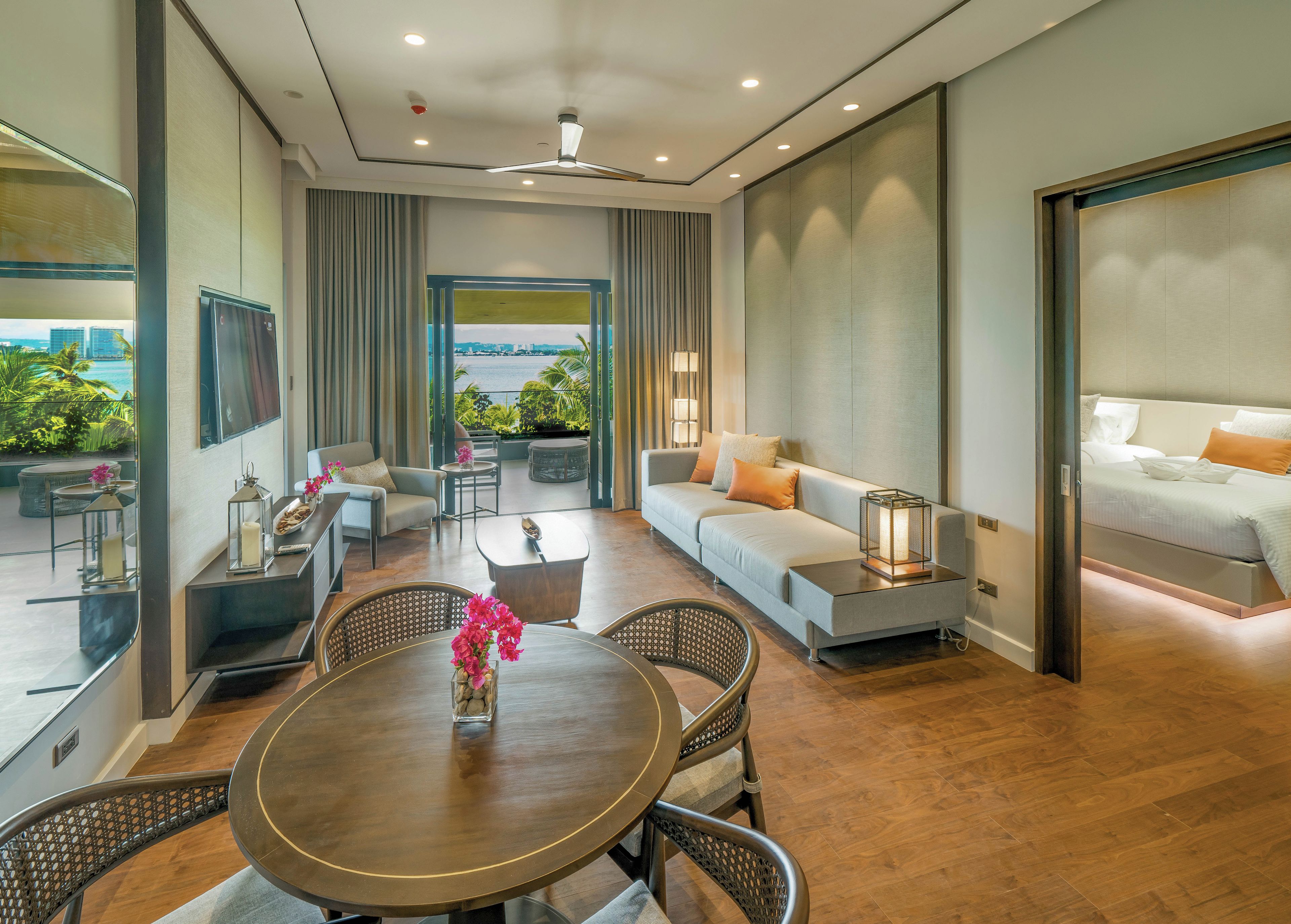 A modern hotel room with a balcony, a sofa, a dining table, and a bed.