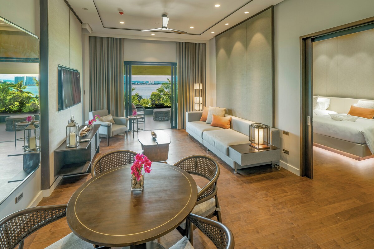 A modern hotel room with a balcony, a sofa, a dining table, and a bed.