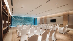 A conference room with rows of white chairs, a stone wall, a television, and wooden shelving. - Discovery Samal (Samal)