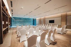 A conference room with rows of white chairs, a stone wall, a television, and wooden shelving. - Discovery Samal (Samal)