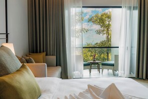Habitación de hotel con una cama grande, un sofá, un balcón con mesa y sillas, y vistas a zonas verdes.