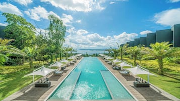 A swimming pool with lounge chairs and umbrellas, surrounded by greenery and a clear sky.