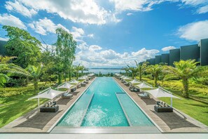 A swimming pool with lounge chairs and umbrellas, surrounded by greenery and a clear sky. - Discovery Samal (Samal)