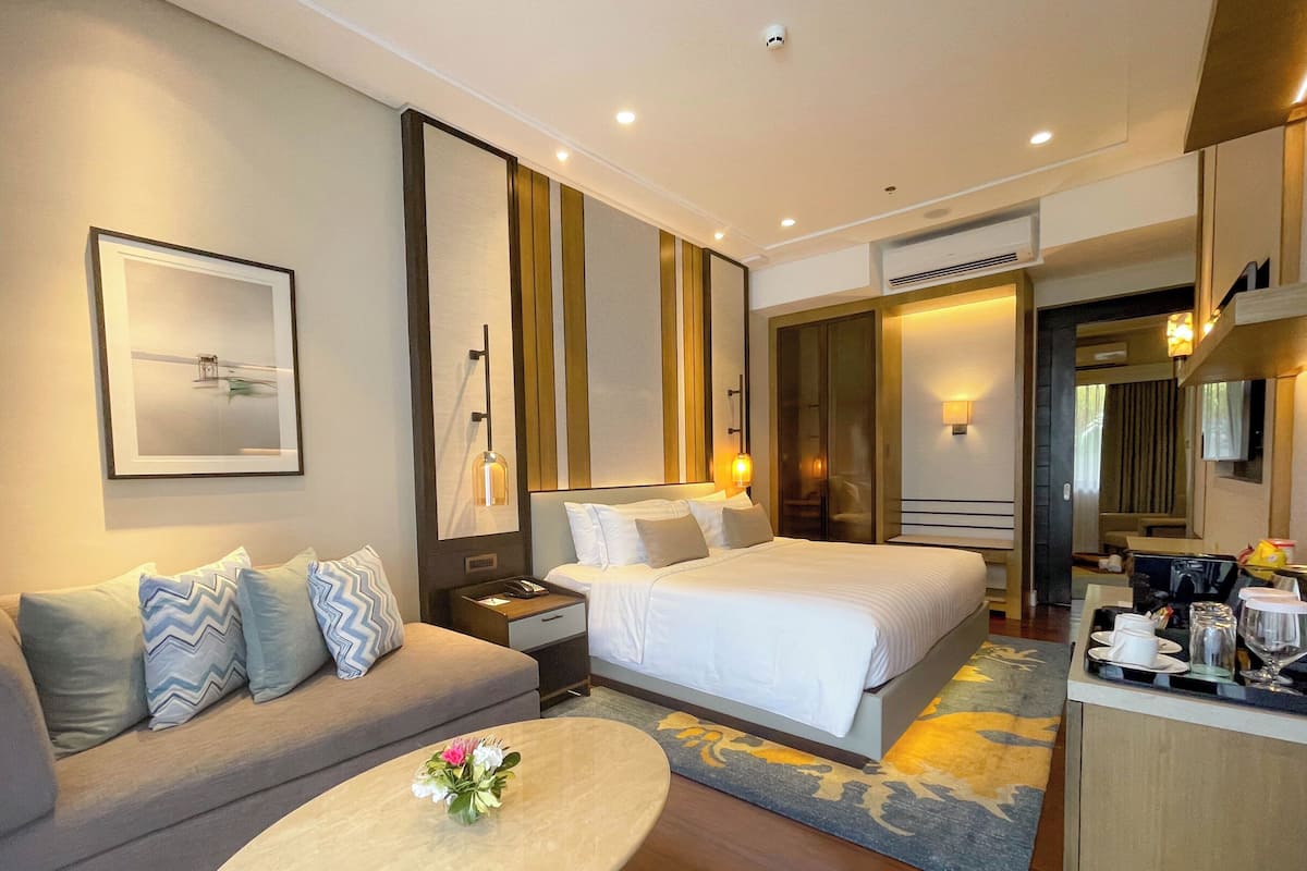 Quarto de hotel com sofá, duas camas, mesa de centro com flores, quadro emoldurado e espelho.