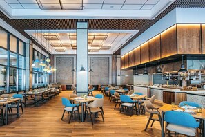 A spacious restaurant with multiple dining tables and chairs, a kitchen area, and large windows allowing natural light. - Discovery Samal (Samal)