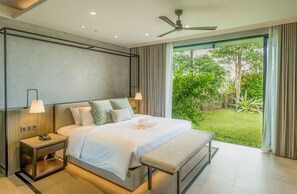 A modern hotel room with a large bed, bedside lamps, a nightstand, a bench, and a view of a lush garden through a sliding glass door. - Discovery Samal (Samal)