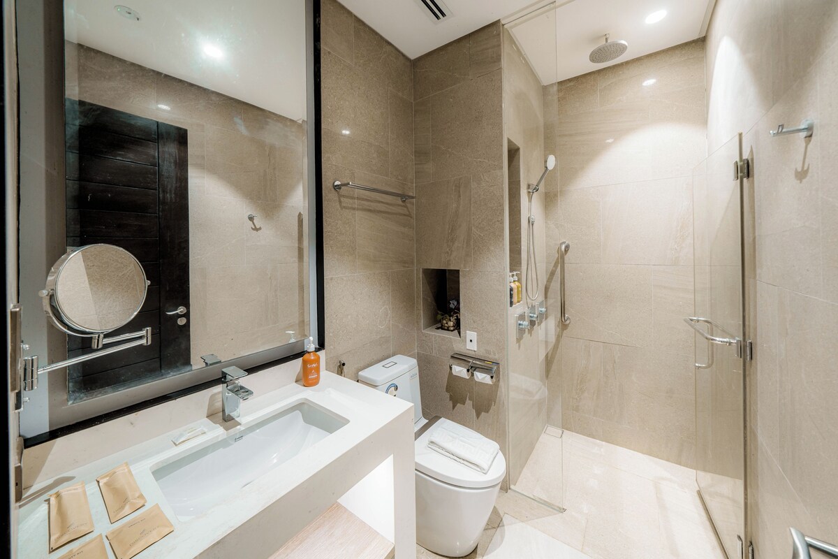 A modern bathroom with a large mirror, a sink, a toilet, and a shower area.