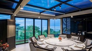Un comedor moderno con una mesa redonda dispuesta para seis, ventanas amplias que ofrecen vistas al exterior y una estructura de techo de cristal.