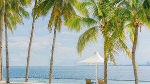 A beach with palm trees, a white umbrella, and two lounge chairs. - Discovery Samal (Samal)